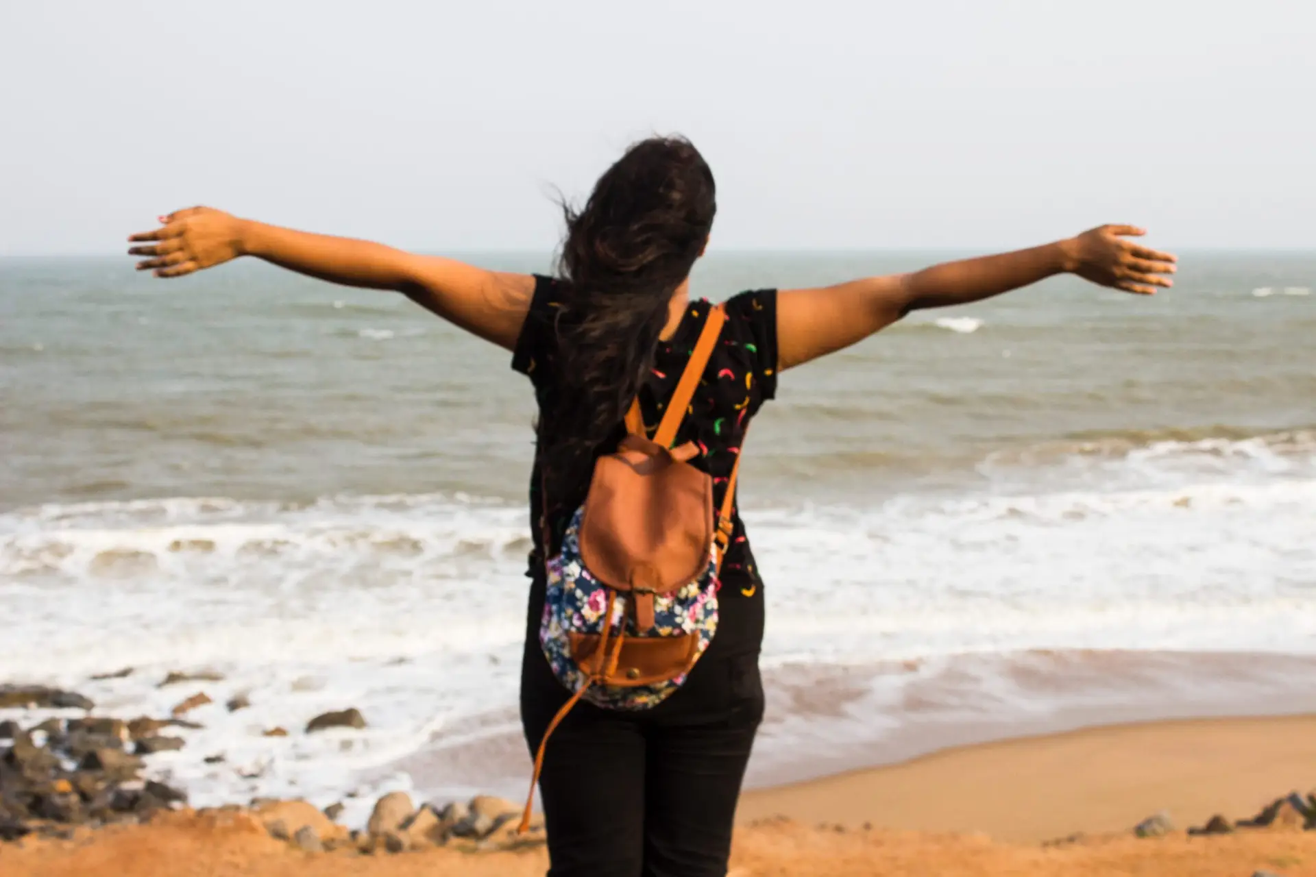 Woman with arms outstretched standing on a beach facing the ocean, embracing freedom and a fresh start.