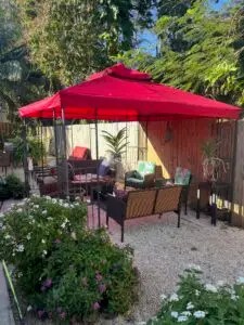 Outdoor seating area with red gazebo, wicker furniture, and tropical plants in a private fenced backyard at a sober living home.