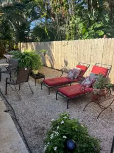 Tranquil outdoor lounge area with red-cushioned chaise chairs, lush plants, and a wood fence at a sober living home.